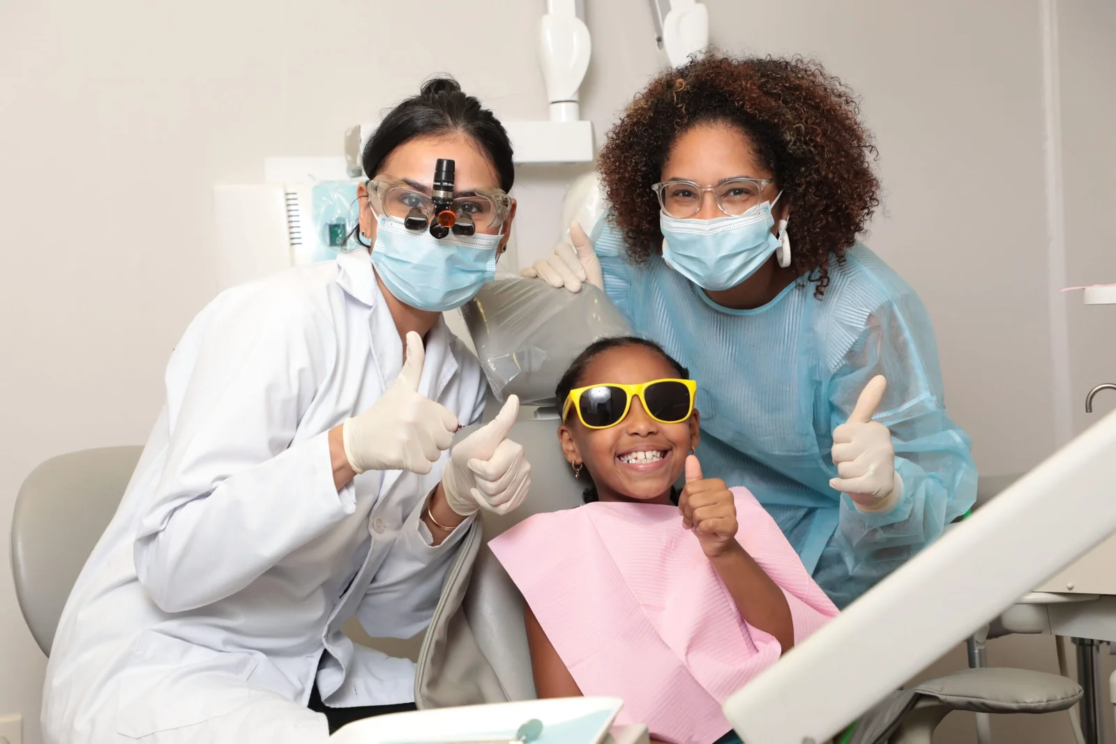 Dr. Jain, dental assistant, and happy child patient giving thumbs up after treatment